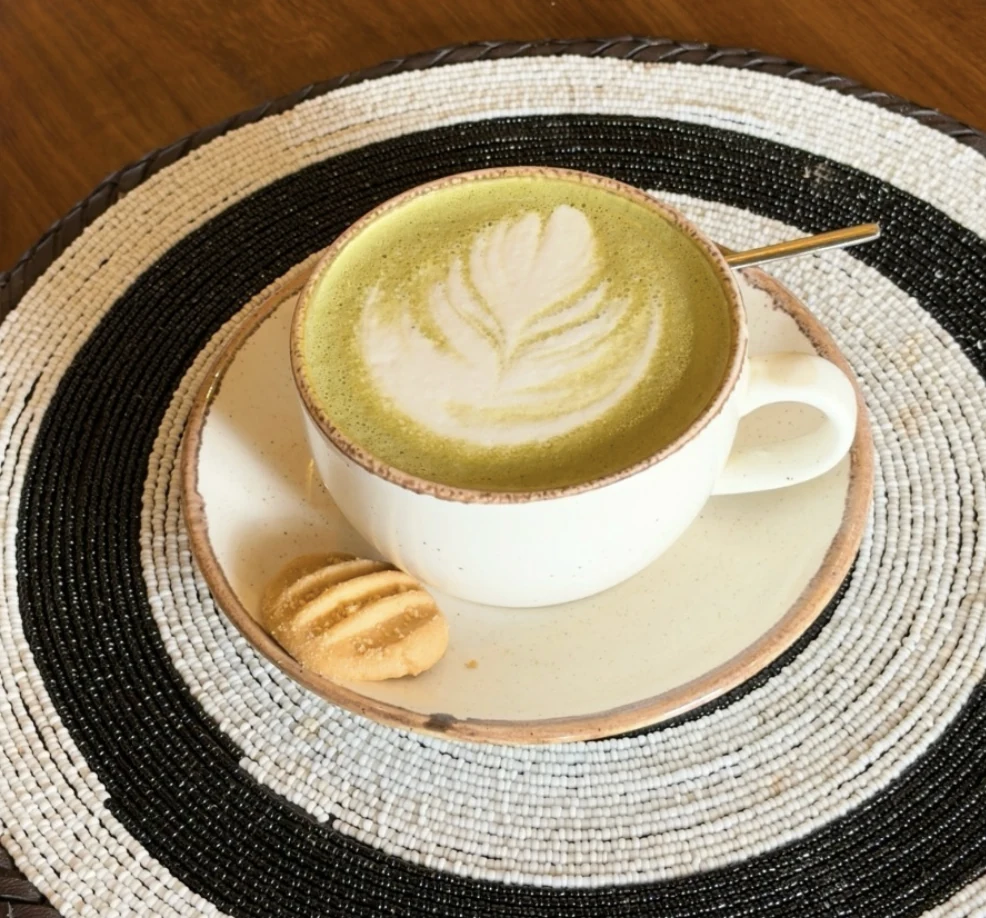 A matcha latte with leaf art on a black and white beaded table setting